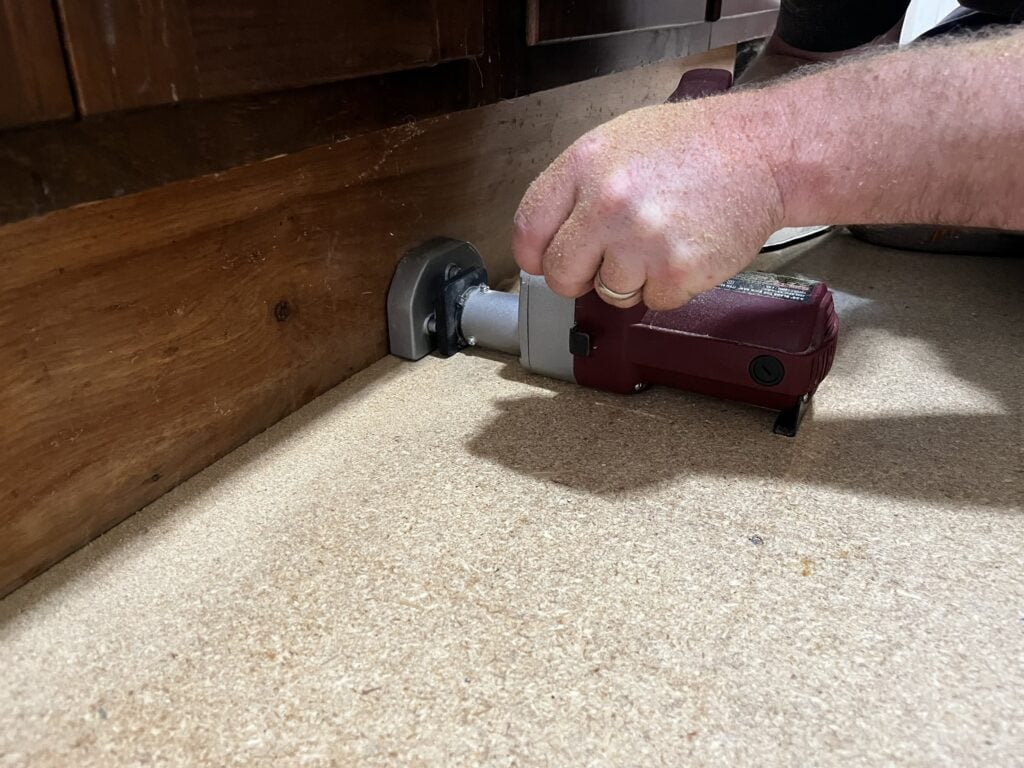 A carpenter using a toe kick saw to cut subfloor flush with kitchen cabinets