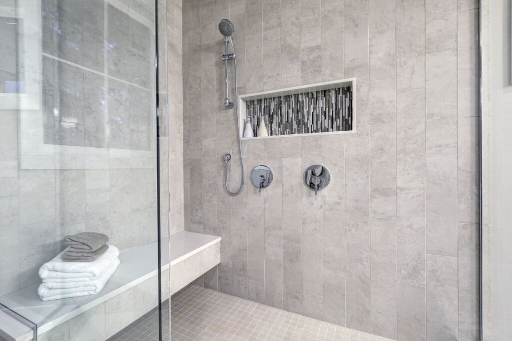 High-end tile shower with a bench, niche, custom shower glass, and diverter valve in a luxury bathroom remodel in Rye, NH