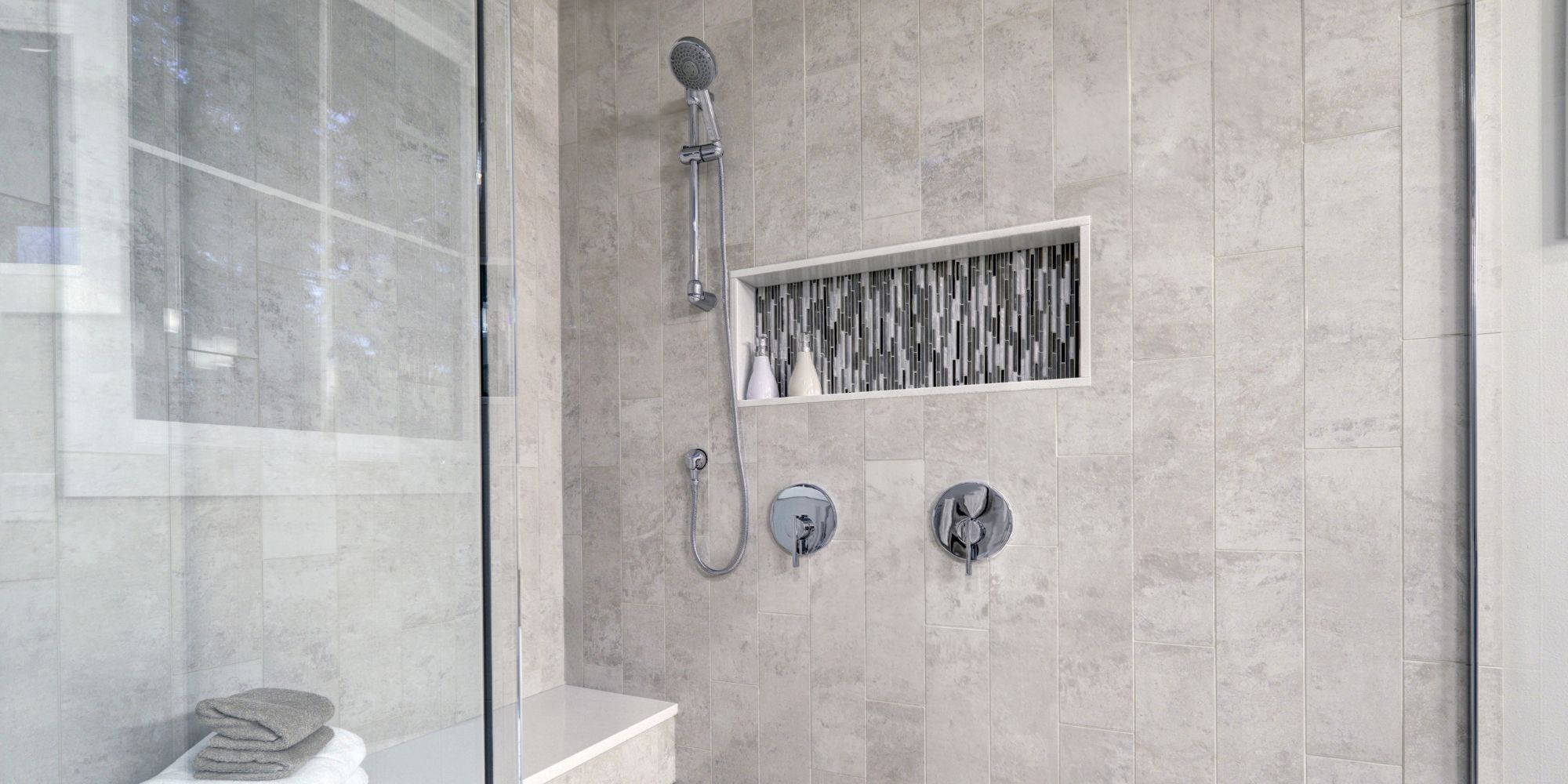 Luxury tile shower replacement in the NH seacoast with a shower niche, custom shower bench, and glass enclosure.
