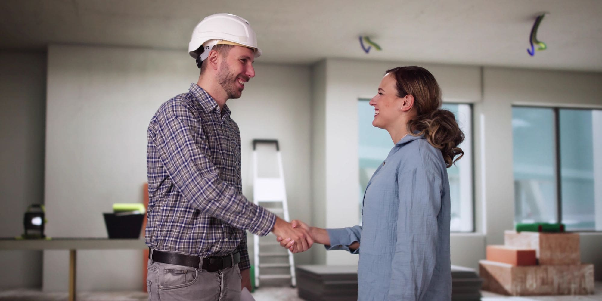 Contractor and a happy homeowner shake hands in a demolished kitchen during a renovation.
